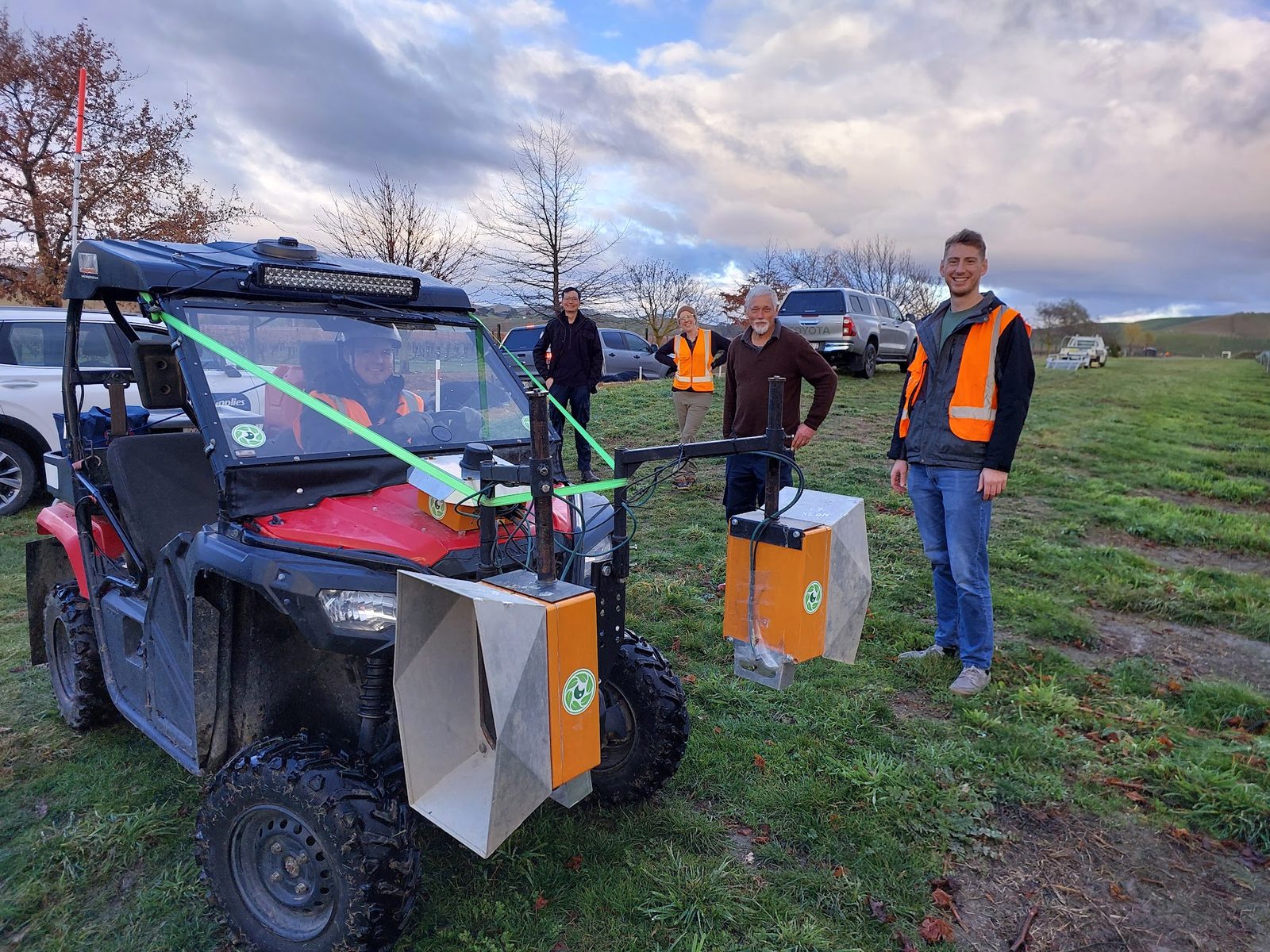 A red Honda side-by-side buggy carrying Cropsy scanner units and white calibration targets, three of the team beside it in a winter vineyard