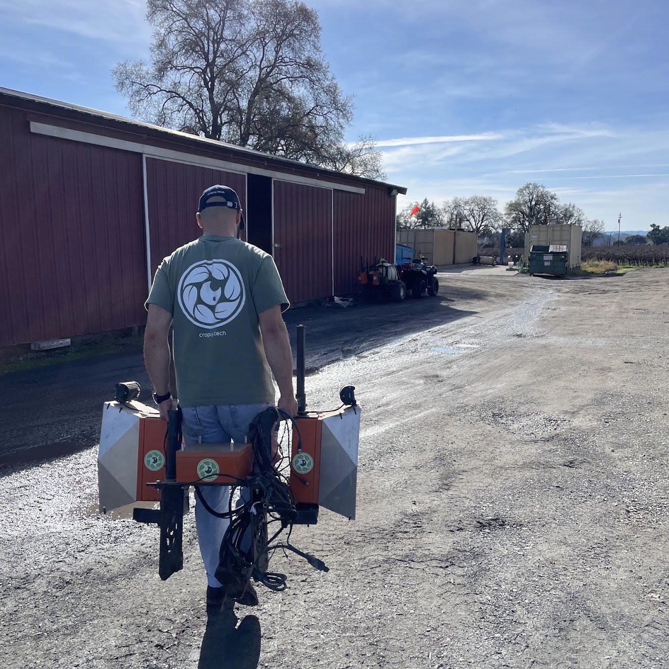 A Cropsy team member carrying a complete scanner rig on a backpack frame across a yard