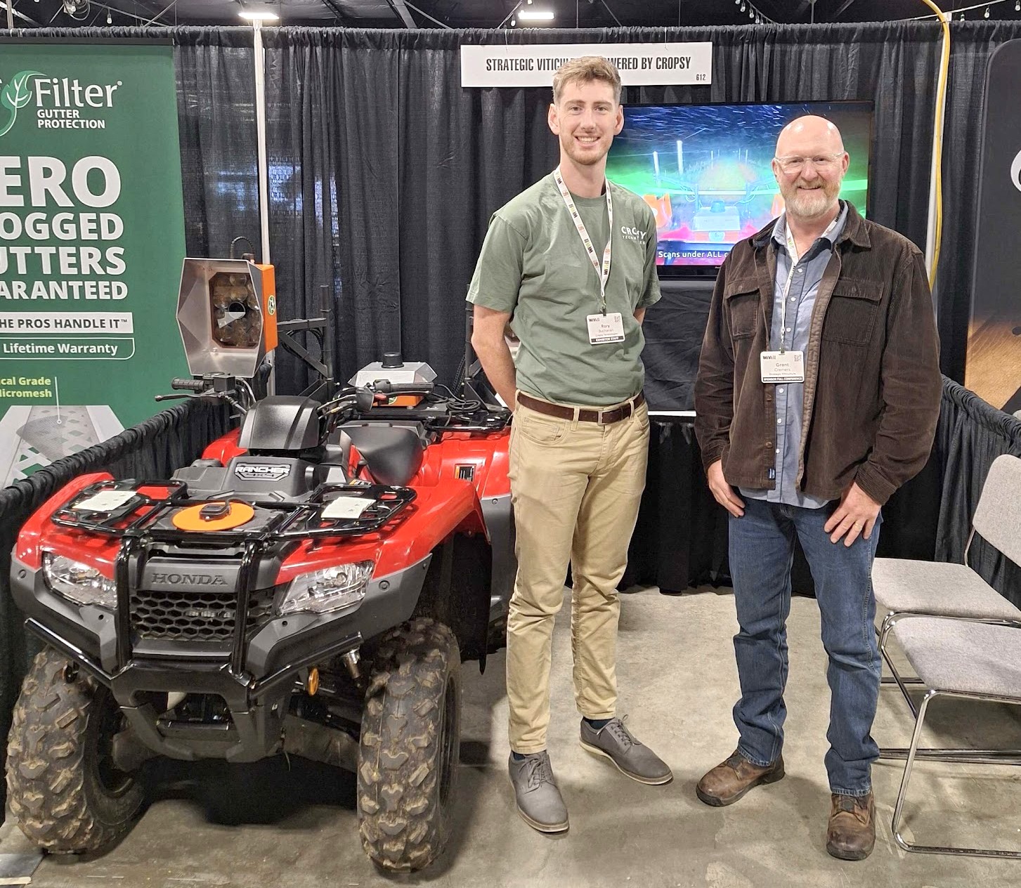 A Honda Rancher quad bike rigged with a Cropsy scanner mount on a trade-show stand, two people beside it under a Strategic Viticulture powered by Cropsy sign