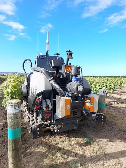 OXIN tracked autonomous vineyard machine straddling a vine row, fitted with orange Cropsy scanner units, antennas and cameras