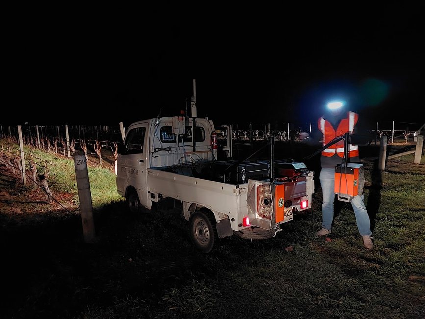 A white Suzuki Carry flatbed parked in a vineyard at night, its Cropsy scanner units lit by their own LED arrays