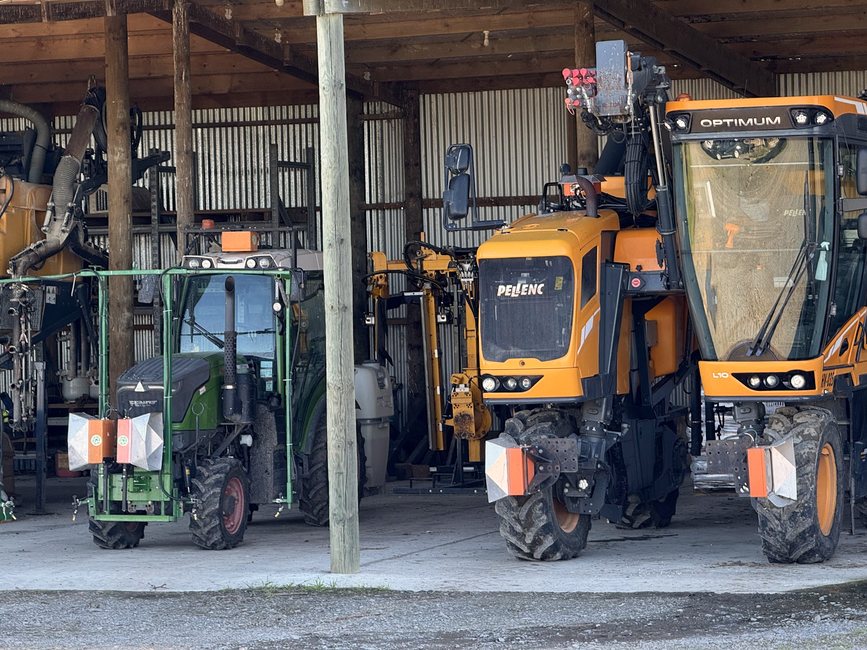 A green Fendt vineyard tractor and a yellow Pellenc Optimum harvester in a shed, both carrying Cropsy scanner units
